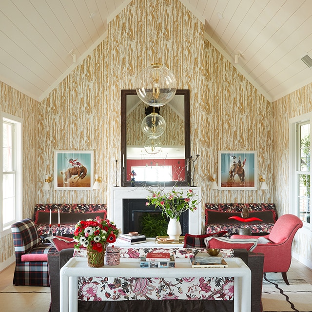 A cheery living room with a vaulted white shiplap ceiling, central fireplace, a plaid couch, and walls in faux-wood design wallpaper.