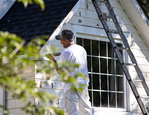 Man in a white shirt repairing the siding of a house.