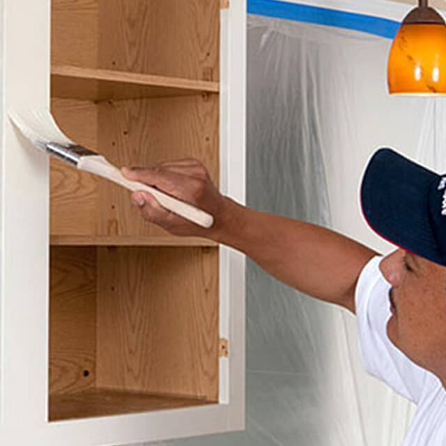 A painting contractor paints a kitchen cabinet.