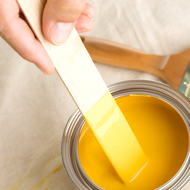 Un bâton à mélanger en bois dans un contenant de peinture jaune