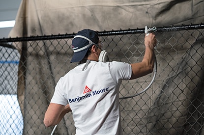 A Benjamin Moore painting contractor spray painting a metal fence using Corotech® COMMAND®.
