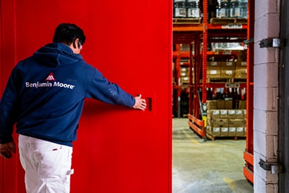 A Benjamin Moore painting contractor opening a large warehouse door painted in Corotech® COMMAND® Safety Red.
