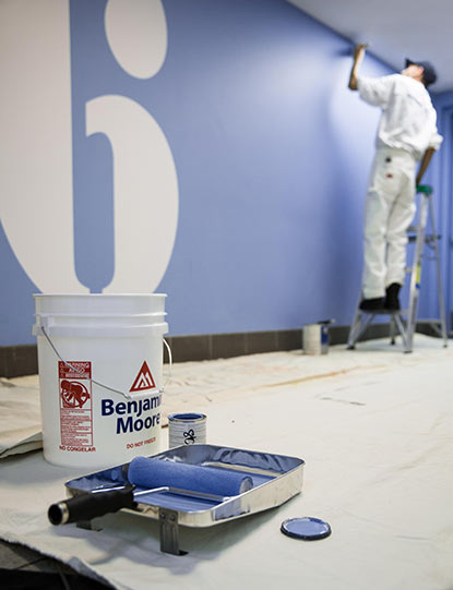 A painting contractor applies blue Benjamin Moore paint tinted with Gennex® Color Technology to a wall.