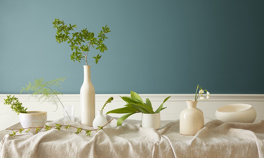 Vases blancs et végétation sur une table devant un mur peint en Vert Antique 2136-40.