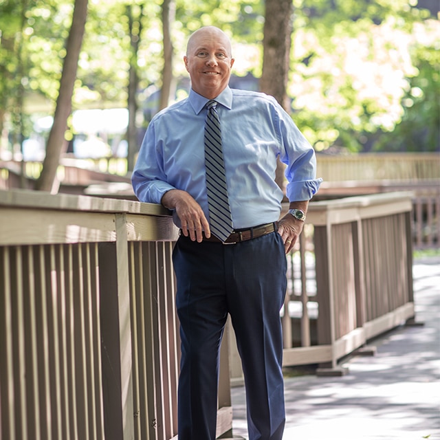 Chairman & CEO of Benjamin Moore, Dan Calkins, standing outside leaning against a wood deck railing.