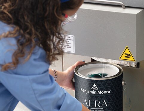 A female lab tech works with an open gallon of Benjamin Moore Aura Interior paint.