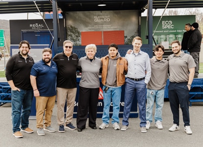 A group of people posing in front of Benjamin Moore outdoor displays with Regal® Select, Element Guard®, and Eco Spec® backdrops. 
