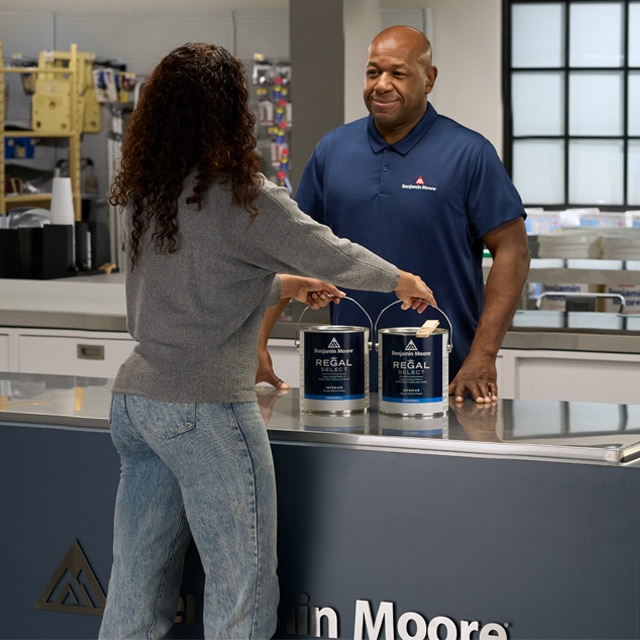 A Benjamin Moore Store professional sells gallons of Regal® Select interior paint to a customer.
