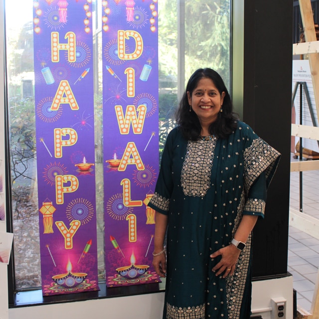 A Benjamin Moore employee dressed in a traditional dress poses beside festive Happy Diwali banners.