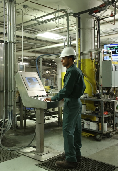 An employee at Benjamin Moore's Newark manufacturing facility wears protective gear and operates machinery during the paint production process.