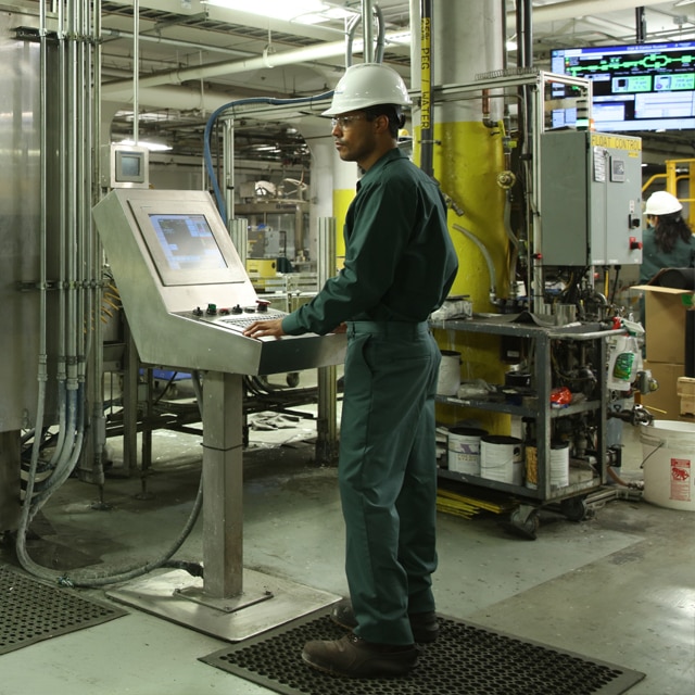 An employee at Benjamin Moore's Newark manufacturing facility wears protective gear and operates machinery during the paint production process.