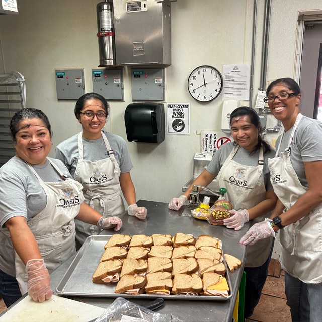 A group of Benjamin Moore employee volunteers in a commercial kitchen posing around a table with a tray of sandwiches.