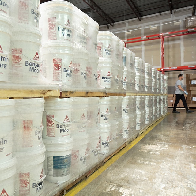 Five gallon containers of Benjamin Moore premium paint in a warehouse.