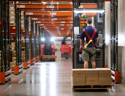Employees drive motorized palette machines in an open warehouse.