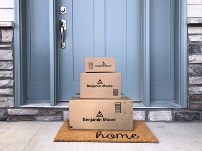 A stack of Benjamin Moore boxes on a welcome mat that says 