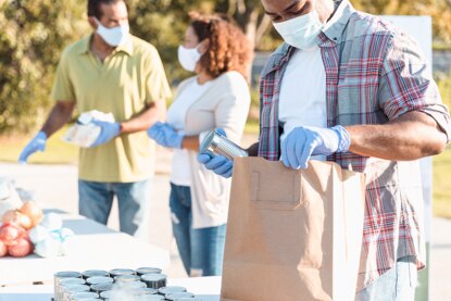 Volunteers provide assistance at an outdoor food bank, filling brown bags with food.
