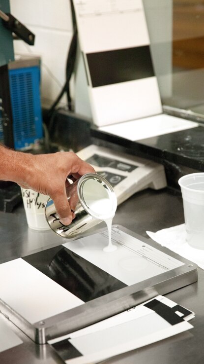 A person pouring white paint into a metal paint tray. A person pouring white paint into a metal paint tray.