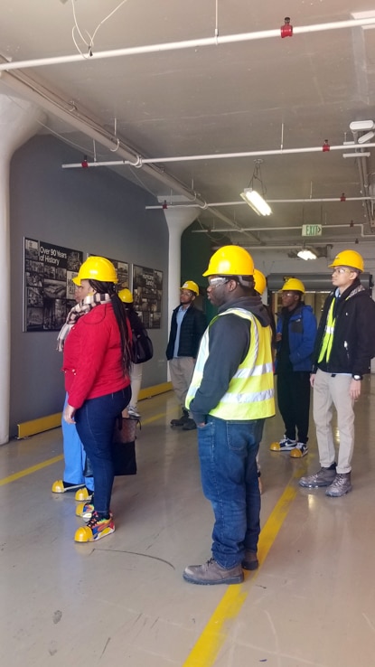 A group of warehouse workers head into the warehouse wearing safety helmets and vests. A group of warehouse workers head into the warehouse wearing safety helmets and vests.