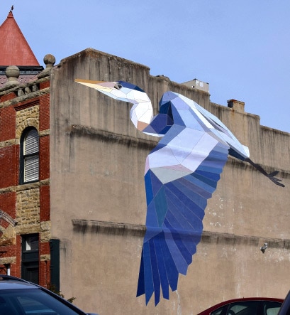 A blue heron flies across a city wall as part of the Mary Lacy Mural Tour.