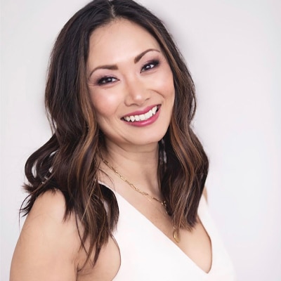 A head shot of a brunette woman with a white sleeveless top.