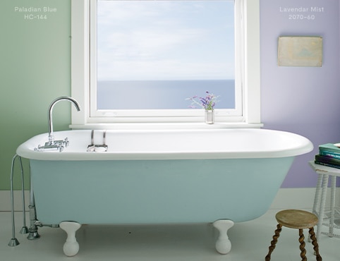 Une salle de bains paisible présentant une baignoire sur pieds bleu clair, un mur peint en vert et un autre peint en violet pastel. 