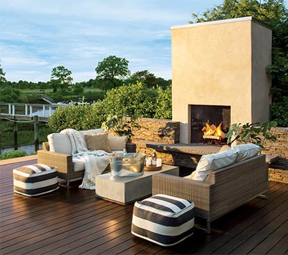 An outdoor deck stained in ARBORCOAT Semi Solid in Cordovan Brown features cushion-covered couches, a bucket of cold drinks and a fireplace.