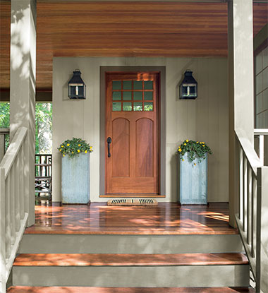 An exterior porch with pillars of yellow flowers features siding and railings stained in ARBORCOAT Solid in Sea Gull Gray, a door and porch floor stained with ARBORCOAT Translucent Cedar, and a ceiling stained in ARBORCOAT Translucent Teak.