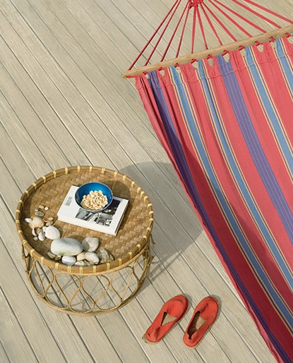 A striped hammock, wicker table and a pair of espadrilles sets a beachy vibe against a neutral deck. A striped hammock, wicker table and a pair of espadrilles sets a beachy vibe against a neutral deck.