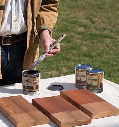 A homeowner using three stain samples of ARBORCOAT on wood to test for color.