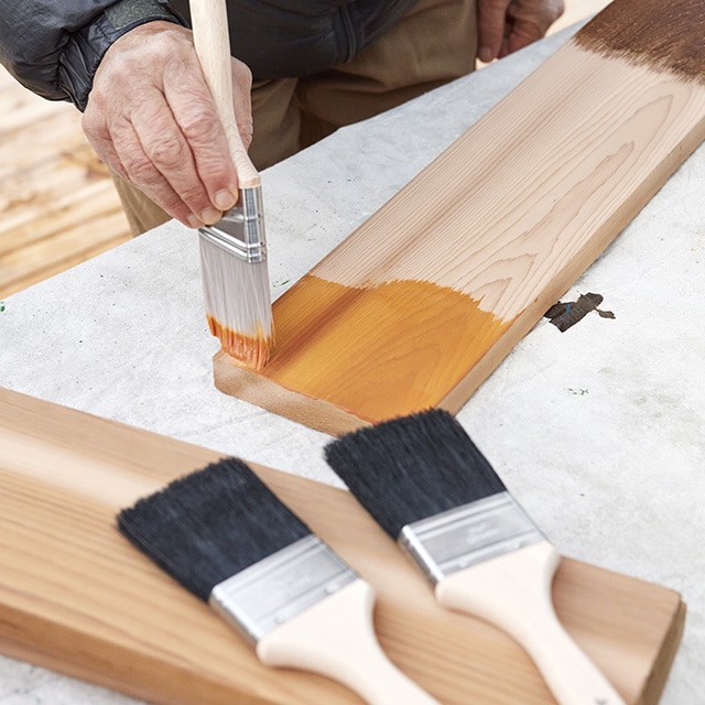Une personne applique des échantillons de teinture Woodluxe au pinceau sur une planche de bois.