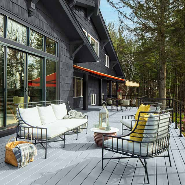 The back of a dark gray exterior sided home with a spacious light gray stained deck and white outdoor furniture.