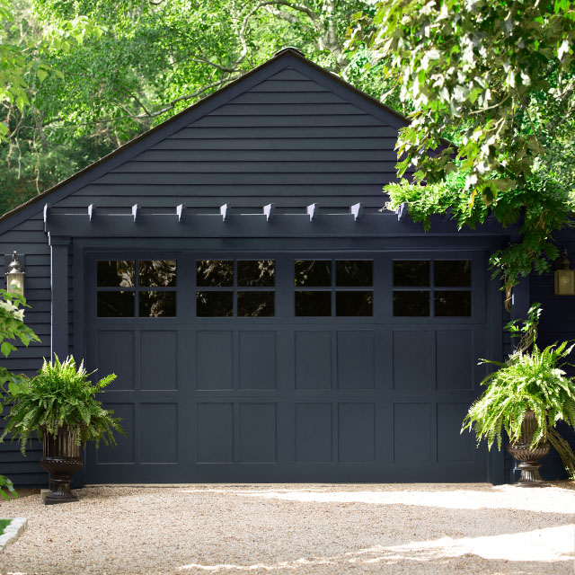 A rich navy blue-painted garage is surrounded by lush greenery.