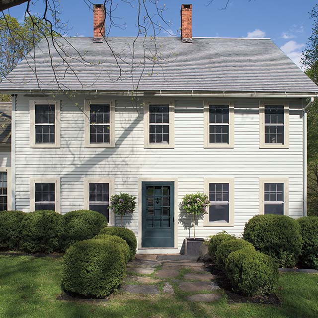 L’extérieur d'une maison de style colonial dite boîte à sel avec des arbustes de chaque côté de l’allée.