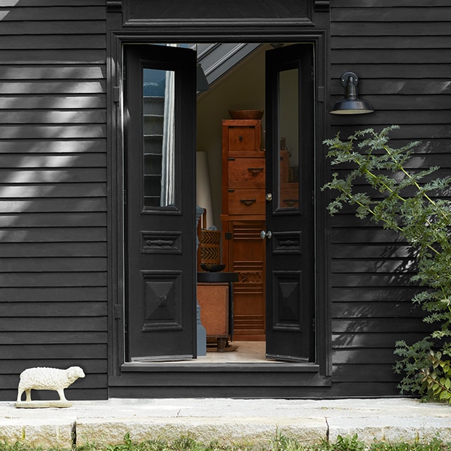A black-painted home exterior, with open, black-painted front doors and trim, and a small decorative lamb statue.