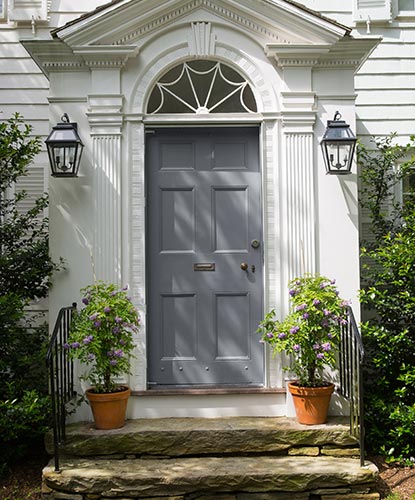 A colonial style front entrance with gray-painted front door and stone steps.