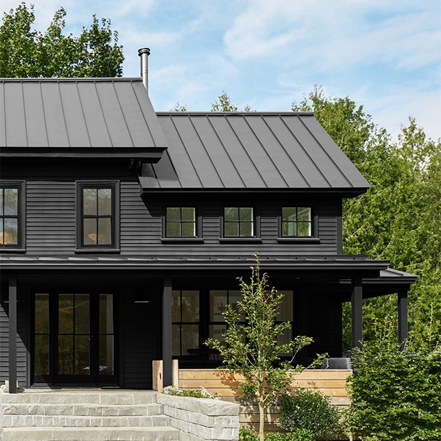 A black-painted house with black trim and front porch, stone steps and greenery.