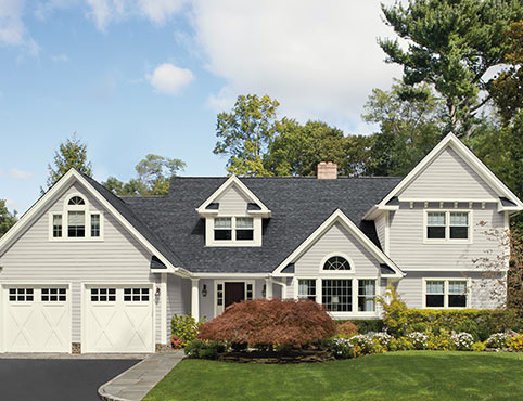 A light gray colored house with vinyl siding and two door garage.