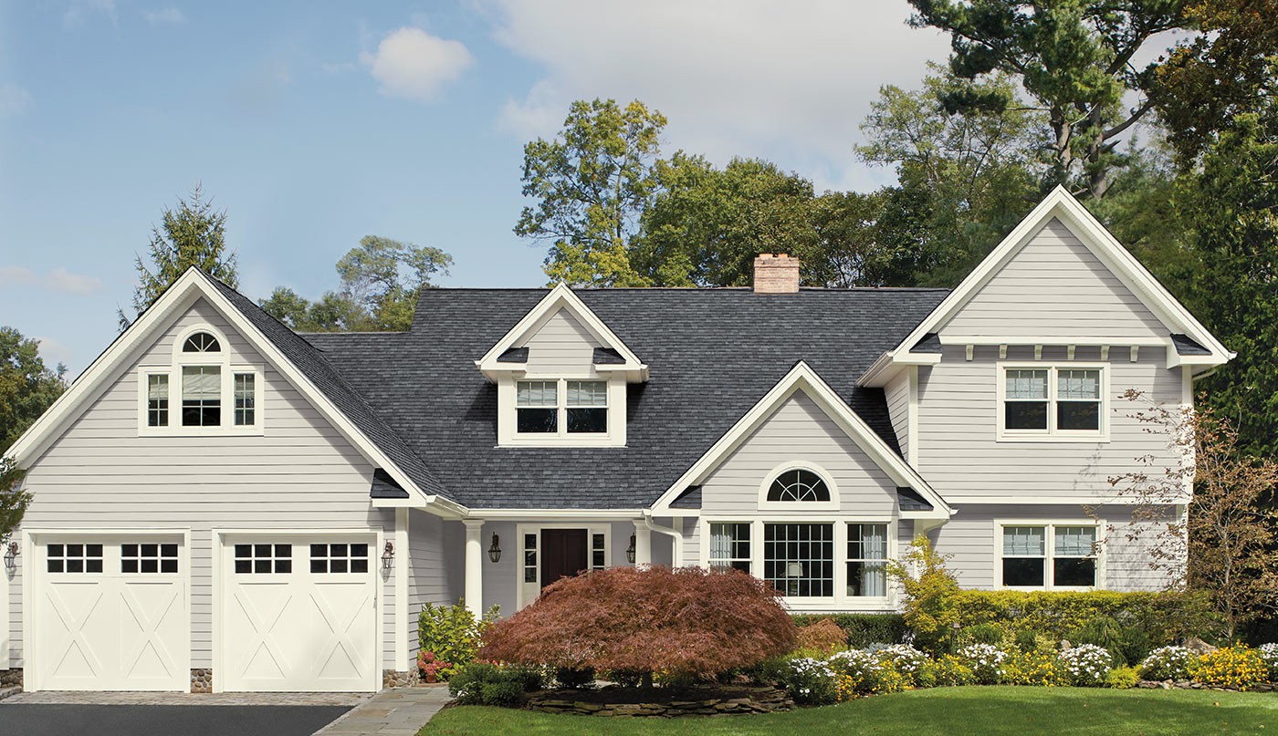 A light gray colored house with vinyl siding and two door garage