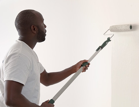 A painting contractor rolling white paint onto a primed wall.