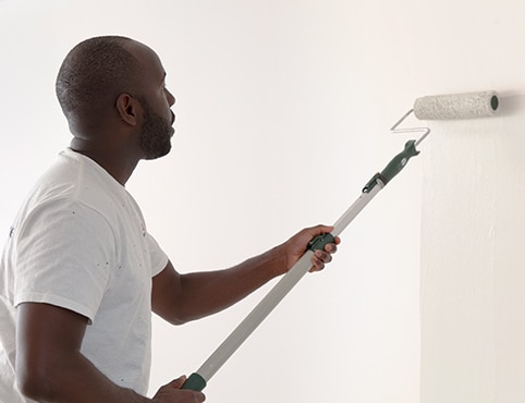 Un contratista de pintura que pinta de blanco con rodillo una pared con imprimador. Un contratista de pintura que pinta de blanco con rodillo una pared con imprimador.