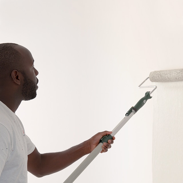 Un peintre applique au rouleau de la peinture blanche sur un mur enduit d’apprêt.