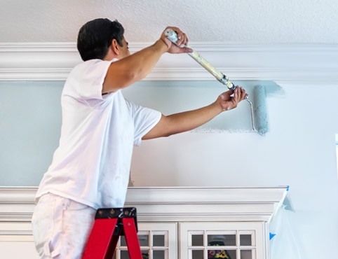 Un contratista de pintura pinta una pared de azul con un rodillo.