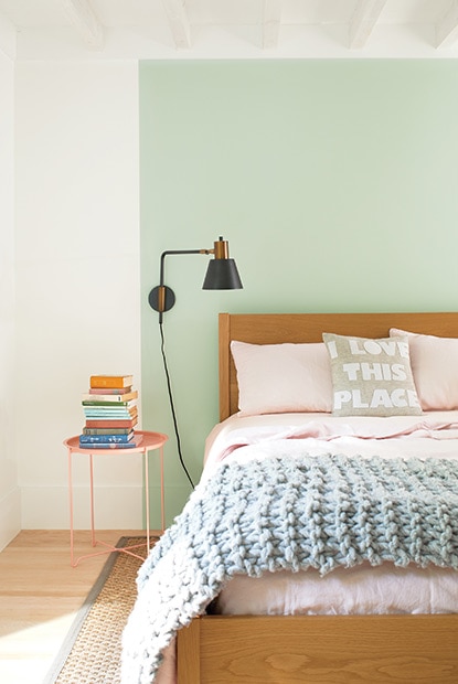 White bedroom with seafoam green color block behind wooden bed with light pink sheets and blue throw blanket.