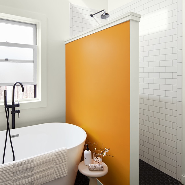 A fun, orange-painted accent wall separates the walk-in shower from a free-standing bathtub in a white painted bathroom with white subway tile.