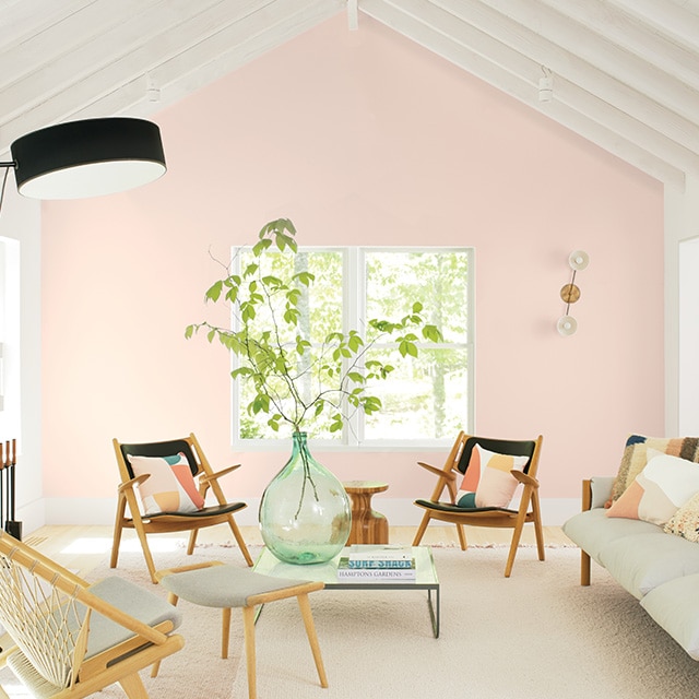 A soft pink-painted accent wall is the highlight of this inviting white painted living room with a vaulted beamed ceiling, fireplace and casual white and black furnishings.