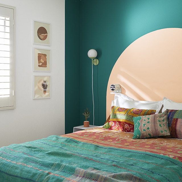 Una habitación blanca con una pared de acento pintada de verde azulado y un arco pintado de durazno detrás de una cama con ropa de cama y cojines de estilo bohemio en verde azulado y Naranja.