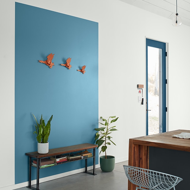 A contemporary white-painted entryway with a blue-trimmed door, and a rich blue-painted rectangle graphic behind a wooden bench, and a wood and charcoal gray-painted island with mesh bar stool.