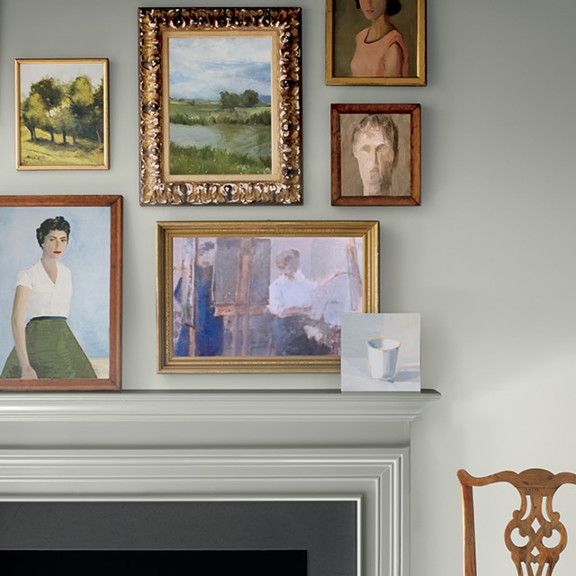 An elegant gray-painted high-gloss fireplace mantel and gray wall, with framed artwork and a wooden chair.