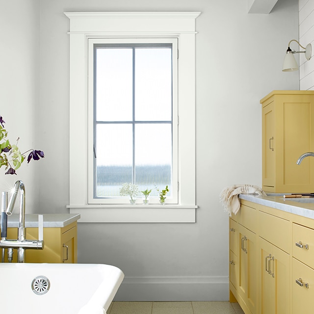 Matte bathroom walls painted in White Heron with yellow-painted cabinets, large tub, and floral accents on window sills.