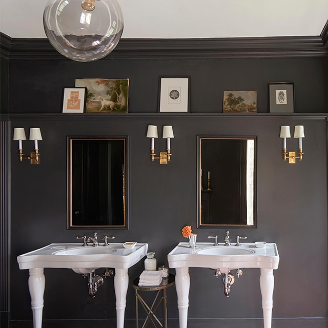 Élégante salle de bains aux moulures et murs noirs avec lavabos blancs, bras de lumière dorés et plafond blanc.